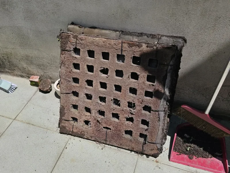 傳統鑄鐵水溝蓋包覆老舊塑膠紗網,外觀殘破且沉重。