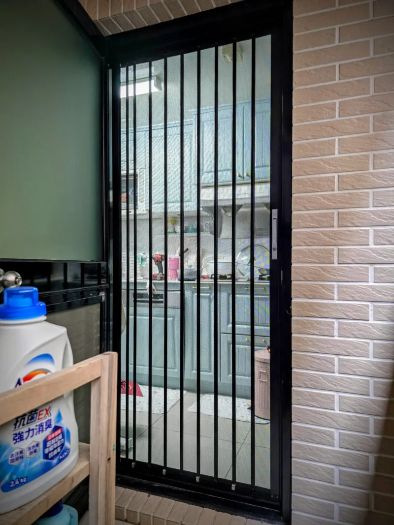 從家事陽台看向廚房內部,展示百摺金紗的外部質感把手與鎖扣細節。平整的門檻與軌道設計,在收納時完全不佔用狹小陽台的進出空間。